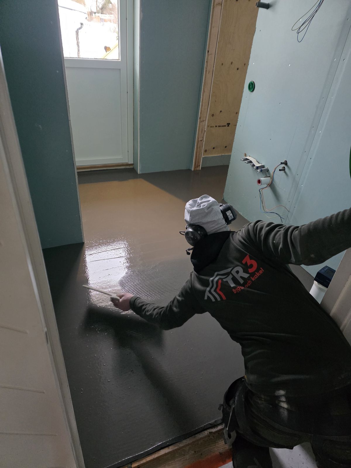 En av oss sprider ut avjämningsmassa på golvet i ett rum som renoveras.